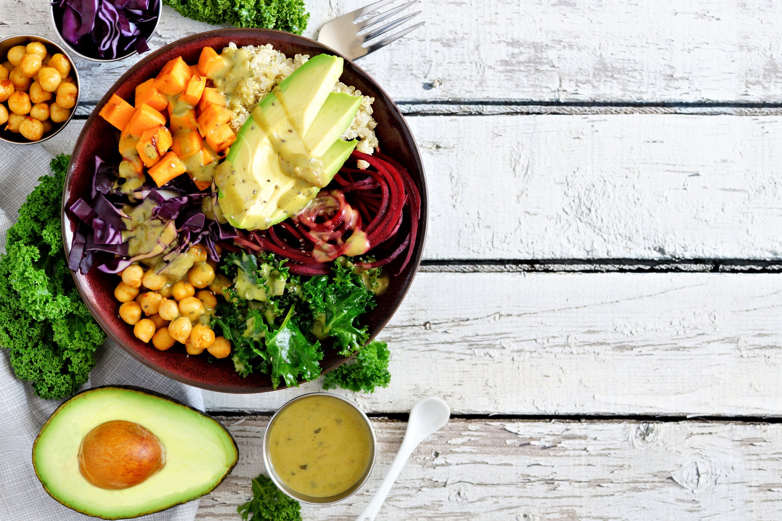 Bowl mit Avocado, Kichererbsen, Salat und verschiedenen Soßen auf einem Holztisch angerichtet