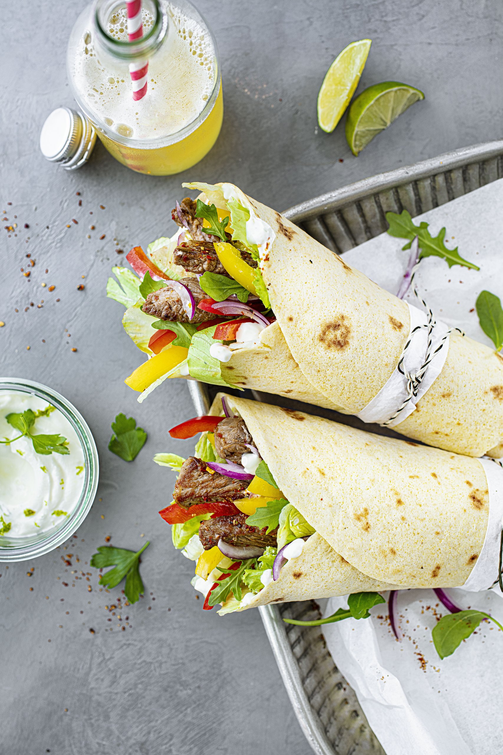 Gesunde Wraps mit Fleisch, Paprika, Zwiebeln und Salat angerichtet mit Kräuterdip und Limonade