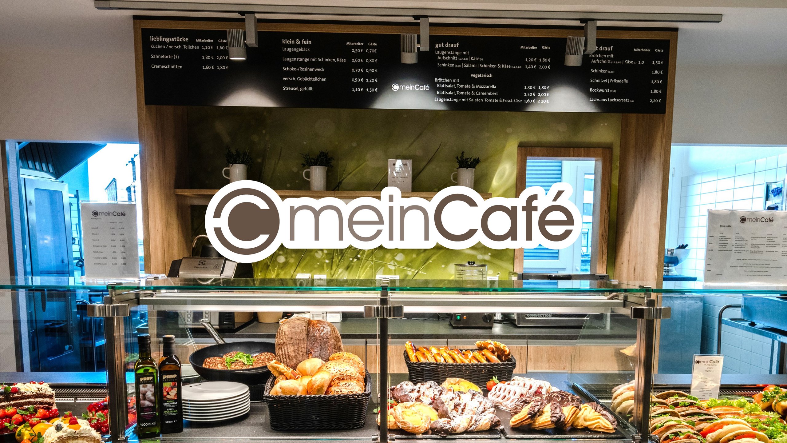 gefüllte Brötchen- und Süßwarentheke, mittig ein braunes "mein Cafe" Logo