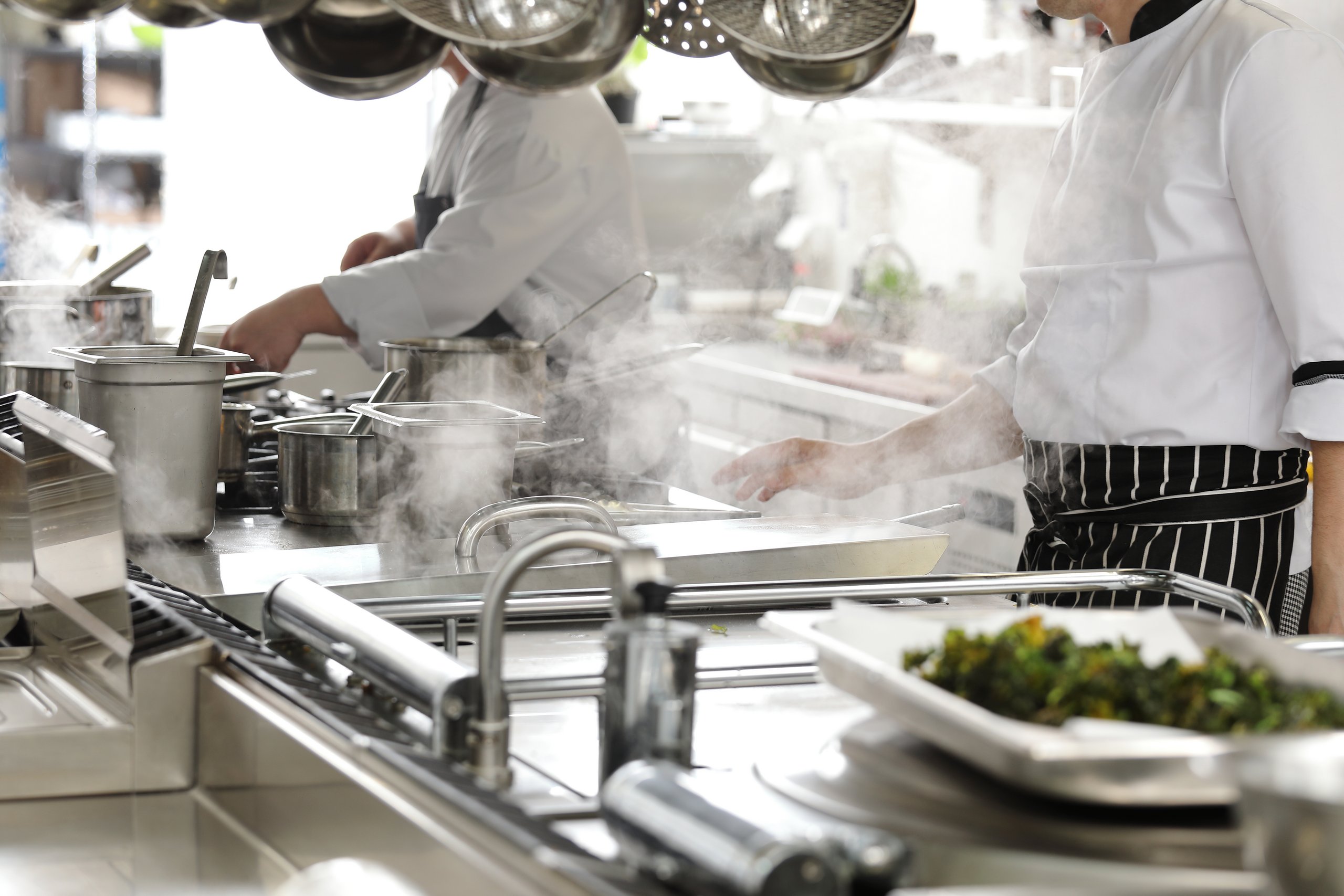 Zwei Köche in schwarz weiß gestreifter Schürze in einer Gastronomie Küche am kochen 