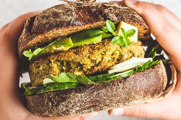 Vegetarischer Burger mit viel Salat und Körnerbrötchen in den Händen einer jungen Frau