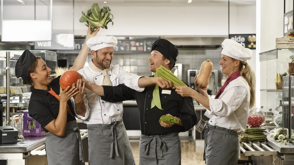 Küchenteam von apetito catering hat Spaß bei der Arbeit, spielt mit frischem Gemüse und freut sich auf die Verpflegung der Gäste und Mitarbeiter 