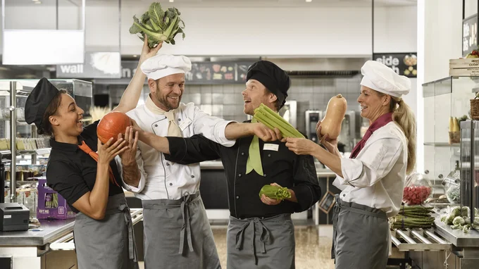 Küchenteam von apetito catering hat Spaß bei der Arbeit, spielt mit frischem Gemüse und freut sich auf die Verpflegung der Gäste und Mitarbeiter 