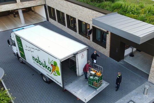 Ein beige, graues Firmengelände. Im Innenhof ein weißer LKW der Firma nabuko. Diese laden Obst und Gemüse aus 