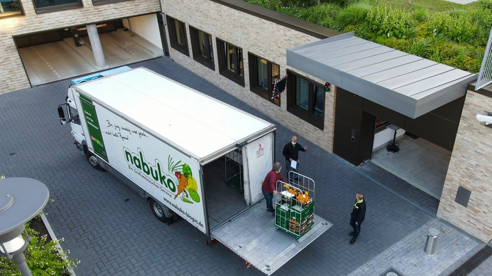 Ein beige, graues Firmengelände. Im Innenhof ein weißer LKW der Firma nabuko. Diese laden Obst und Gemüse aus 