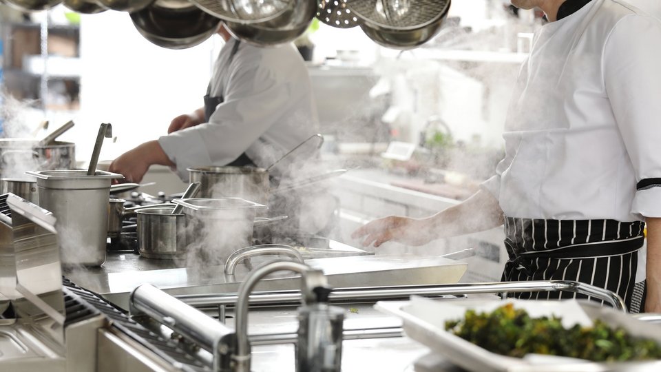 Zwei Köche in schwarz weiß gestreifter Schürze in einer Gastronomie Küche am kochen 