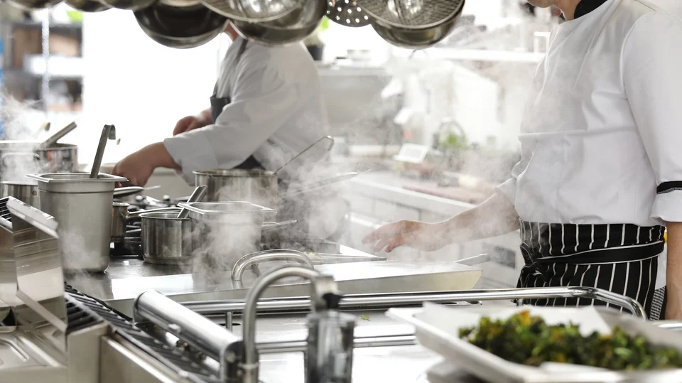 Zwei Köche in schwarz weiß gestreifter Schürze in einer Gastronomie Küche am kochen 